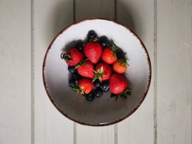 Parlak tabakta taze çilek ve yabanmersini.