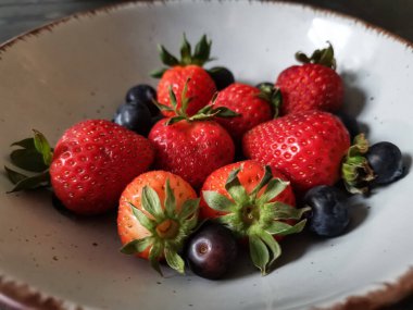 Parlak tabakta taze çilek ve yabanmersini.