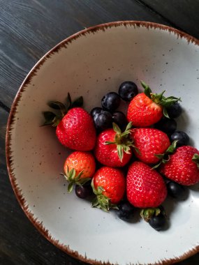 Parlak tabakta taze çilek ve yabanmersini.