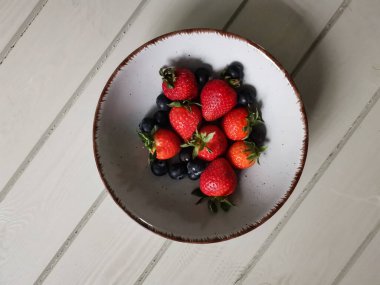 Parlak tabakta taze çilek ve yabanmersini.