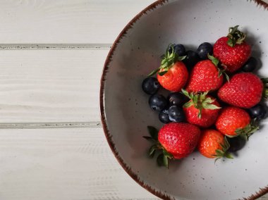 Parlak tabakta taze çilek ve yabanmersini.