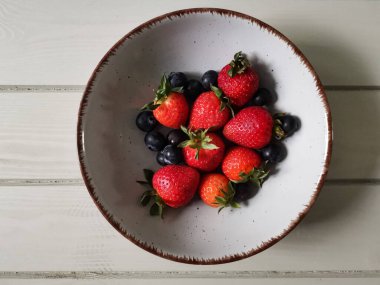 Parlak tabakta taze çilek ve yabanmersini.