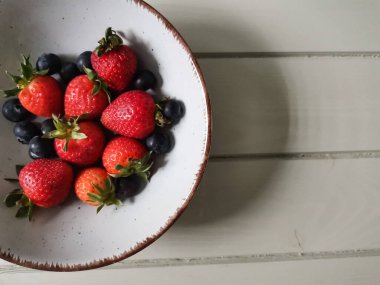 Parlak tabakta taze çilek ve yabanmersini.
