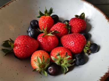 Parlak tabakta taze çilek ve yabanmersini.