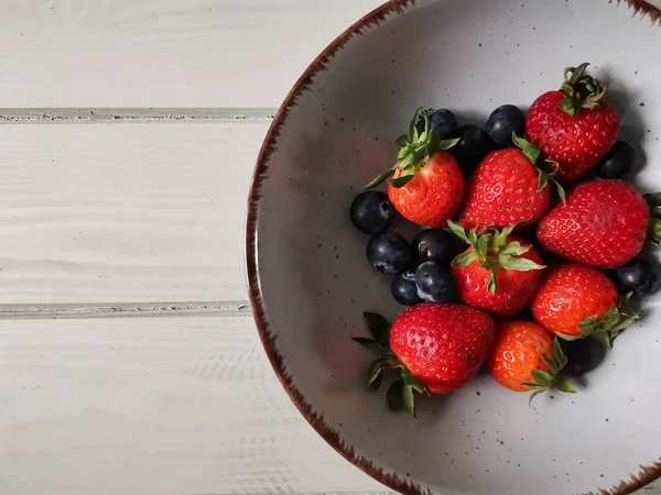 Parlak tabakta taze çilek ve yabanmersini.