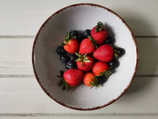 Parlak tabakta taze çilek ve yabanmersini.
