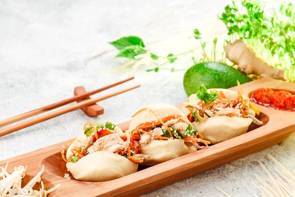 Comida tradicional panasiática. Bao - pastel al vapor con relleno de carne y verduras frescas en el plato de madera con palillos chinos. Fondo de hormigón. Espacio para texto — Foto de Stock