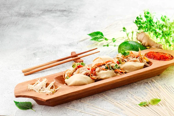 Traditional pan-asian food. Bao - steamed pie with meat filling and fresh vegetables on wooden plate with chinese chopsticks. Concrete background. Space for text