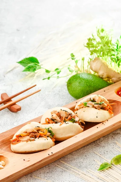 Comida tradicional panasiática. Bao - pastel al vapor con relleno de carne y verduras frescas en el plato de madera con palillos chinos. Fondo de hormigón. Espacio para texto — Foto de Stock