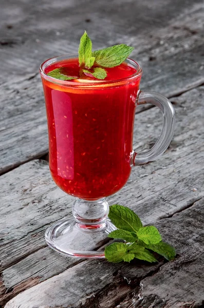Classic raspberry tea with mint in a glass on a rustic wooden background. Space for text. Photo for menus and advertising
