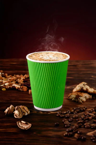 Café con nueces en taza de papel verde sobre fondo de madera. Burlarse. Cappuccino llevar. Espacio para texto. — Foto de Stock
