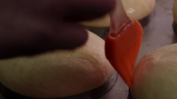 Processo di fabbricazione del pane rotondo. Panettiere applicare tuorli sulla pasta cruda con pennello da pasticceria. Da vicino. — Video Stock
