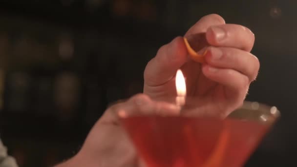 Barmen kırmızı bir kokteyli portakal kabuğuyla süslüyor. Zarif bardakta kokteyl.. — Stok video