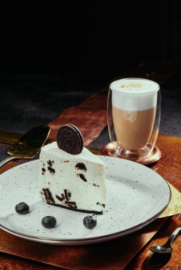 Oreo peynirli kek. Krem kapaklı cheesecake ve bakır kaplamalı beyaz tabakta çikolatalı kurabiyeler. Kapat.