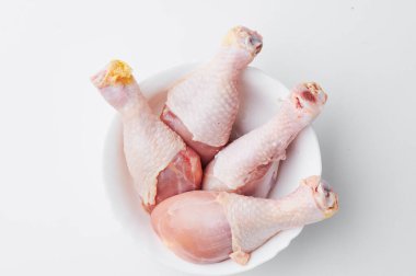 Beyaz arka planda izole edilmiş beyaz bir tabakta çiğ tavuk bacağı. Yakın plan. Model