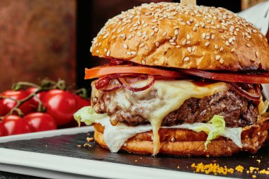 Büyük burger, sulu pirzola, peynir, domates, marul, patates kızartması ve barbekü sosuyla servis edilen bakır tabaklar. Kapat.