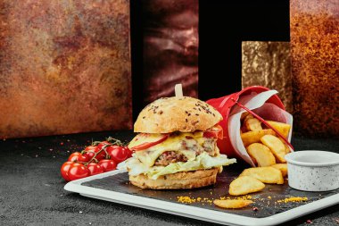 Büyük hamburger, sulu pirzola, peynir, domates, bakır tabakların arka planında siyah bir tabakta marul. Kapat. makro