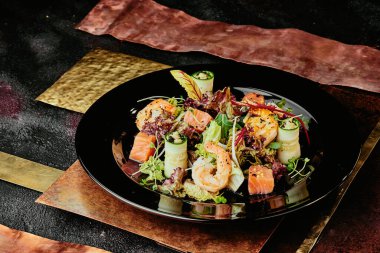 Somonlu salata, karides, marul, salatalık ve soya filizleri bakır tabaklarda siyah bir tabakta. Kapat.