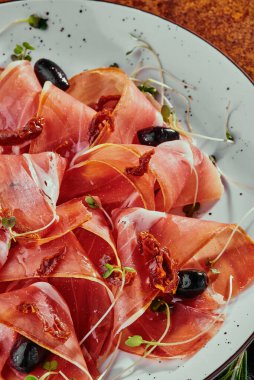 Jamonlu soğuk tütsülenmiş et tabağı, beyaz tabakta zeytin ve soya fasulyesi filizi ve bakır arka planda ızgara sebze. Üst Manzara. Kapat.