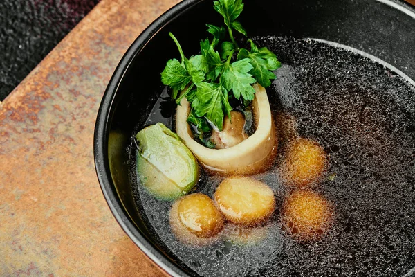 Kemikli şeffaf et suyu, maydanozla süslenmiş ve bakır arka planda siyah bir kasede Brüksel lahanası. Menü için. Bir dizi fotoğraf. yakın plan.