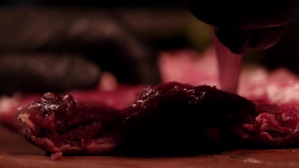 A séf nyers marhahúsos szűzpecsenyét szeletel egy fa deszkán. Márványhús. Sötét légkör — Stock videók