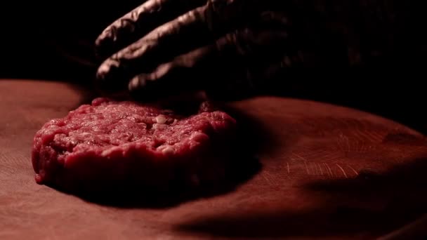 Chef en guantes negros hace una chuleta de carne picada cruda. Carne de mármol. Ambiente oscuro. — Vídeos de Stock