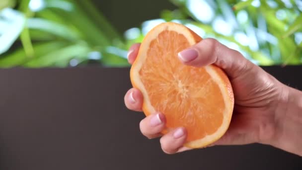 Squeeze juice from orange. Woman hand squeezes half orange on a tropical background. Slow Motion — Stock Video