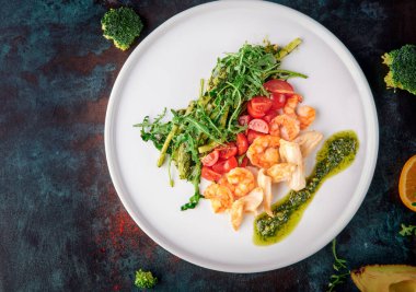 Karidesli salata, tavuk, vişneli domates ve mavi oksitlenmiş arka planda beyaz tabakta roka.