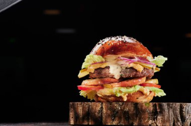 Peynirli sığır burger, ızgara sebze, domates, kırmızı soğan ve siyah arka planda ahşap kesim marul. Mesaj için yer var. Sağlıksız yiyecekler.