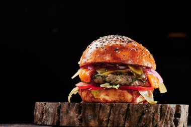 Peynirli sığır burger, domates, kırmızı soğan, salatalık ve marul, siyah arka planda. Mesaj için yer var. Sağlıksız yiyecekler.