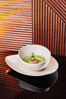 Güzel beyaz bir tabakta domates ve mantarla süslenmiş yeşil kremalı ıspanak çorbası.