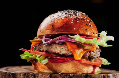 Peynirli sığır burger, domates, kırmızı soğan, salatalık ve marul, siyah arka planda. Hamburger menüsü. Mesaj için yer var. Sağlıksız yiyecekler.