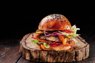 Peynirli sığır burger, domates, kırmızı soğan, salatalık ve marul, siyah arka planda. Hamburger menüsü. Mesaj için yer var. Sağlıksız yiyecekler.