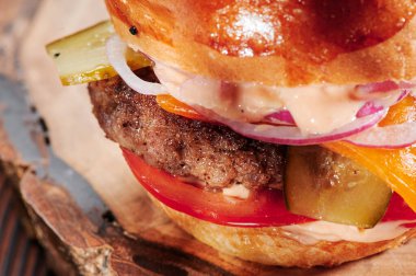 Peynirli sığır burger, domates, kırmızı soğan, salatalık ve marul, siyah arka planda. Mesaj için yer var. Sağlıksız yiyecekler.