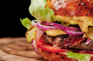 Peynirli sığır burger, domates, kırmızı soğan, salatalık ve marul. Kapatın. Sağlıksız yiyecekler