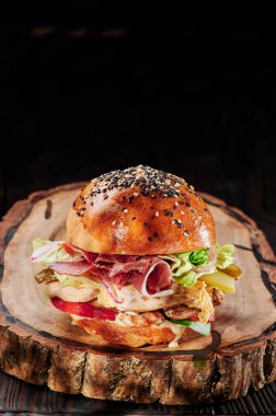 Tavuk ve pastırmalı sulu burger, peynir, domates, ahşap kesikli marul ve siyah arka plan. Hamburger menüsü. Metin için boşluk.