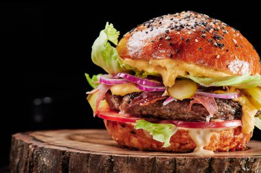 Peynirli sığır burger, domates, kırmızı soğan, salatalık ve marul, siyah arka planda. Mesaj için yer var. Sağlıksız yiyecekler.