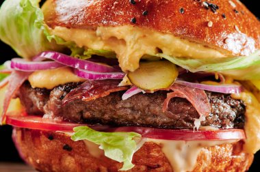 Peynirli sığır burger, domates, kırmızı soğan, salatalık ve marul. Kapatın. Sağlıksız yiyecekler