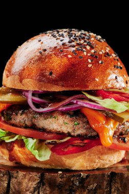Peynirli sığır burger, domates, kırmızı soğan, salatalık ve marul, siyah arka planda. Hamburger menüsü. Mesaj için yer var. Sağlıksız yiyecekler.