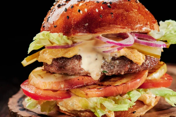 Marha burger sajttal, grill zöldség, paradicsom, vöröshagyma és saláta fa vágott fekete alapon. Helyet a szövegnek. Egészségtelen élelmiszer. — Stock Fotó