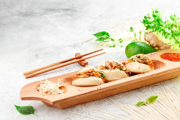 Traditional pan-asian food. Bao - steamed pie with meat filling and fresh vegetables on wooden plate with chinese chopsticks. Concrete background. Space for text