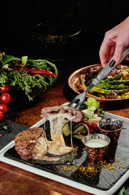 İçinde peynir olan et pirzolası ve siyah tabakta ızgara sebze. Bakır arka plan. Kapat.