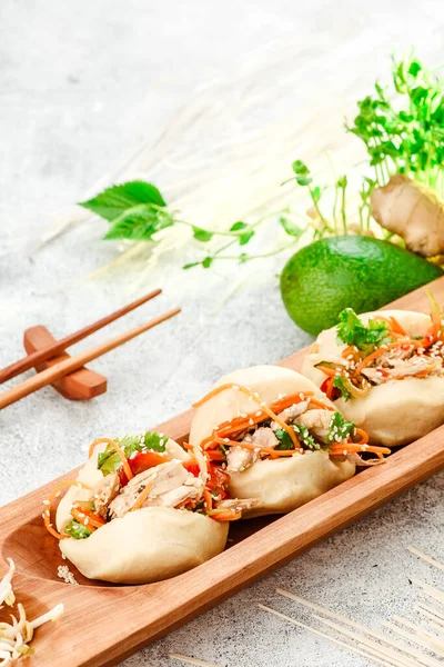 Traditional pan-asian food. Bao - steamed pie with meat filling and fresh vegetables on wooden plate with chinese chopsticks. Concrete background. Space for text