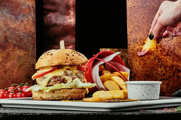 Großer Burger mit saftigen Schnitzeln, Käse, Tomaten, Salat auf einem schwarzen Teller auf dem Hintergrund von Kupfertellern. Nahaufnahme. Makro — Stockfoto