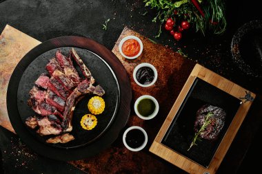 Mayalanmış biftek. Siyah yuvarlak tabakta ızgara sebzeli T-Bone bifteği ve bakır bir çarşaf. Üst Manzara. Metin için boşluk