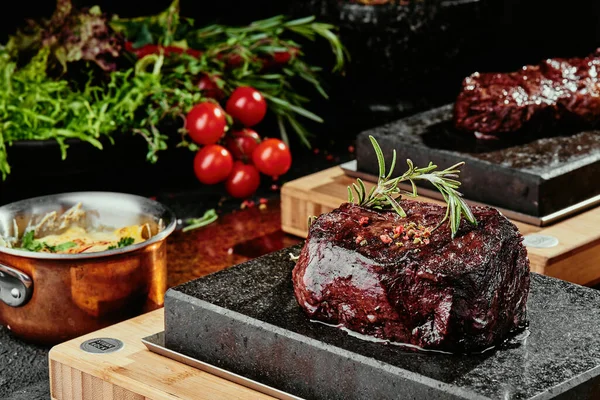 Grilovaný steak. Filet Mignona na černém talíři na pozadí zeleně, koření a zeleniny, na měděném plechu. zavřít — Stock fotografie