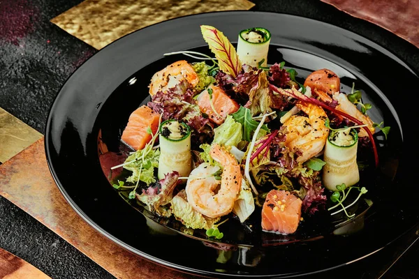 Somonlu salata, karides, marul, salatalık ve soya filizleri bakır tabaklarda siyah bir tabakta. Kapat.