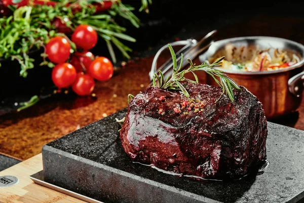 Grilovaný steak. Filet Mignona na černém talíři na pozadí zeleně, koření a zeleniny, na měděném plechu. zavřít — Stock fotografie