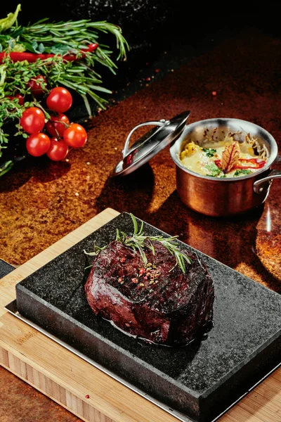 Grilovaný steak. Filet Mignona na černém talíři na pozadí zeleně, koření a zeleniny, na měděném plechu. zavřít — Stock fotografie