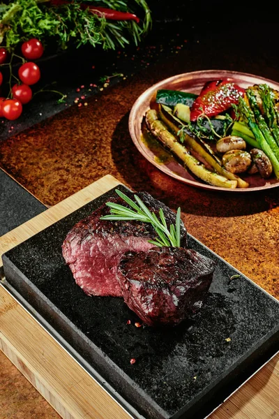Kvašený steak. Grilované steakové médium s grilovanou zeleninou na černém podnose na měděném podkladu. Zblízka. série fotografií — Stock fotografie